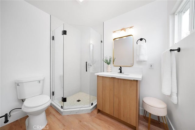 bathroom with toilet, a stall shower, wood finished floors, baseboards, and vanity