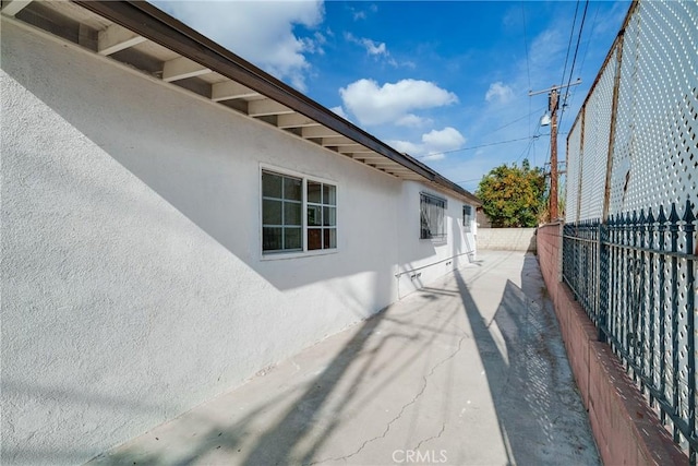 view of side of property with stucco siding, a patio, and fence