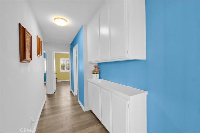 corridor with attic access, light wood-style floors, and baseboards