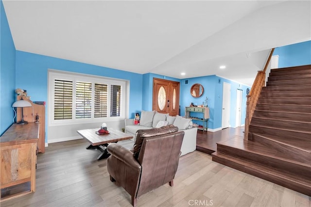 living area with light wood-type flooring, stairway, lofted ceiling, and baseboards