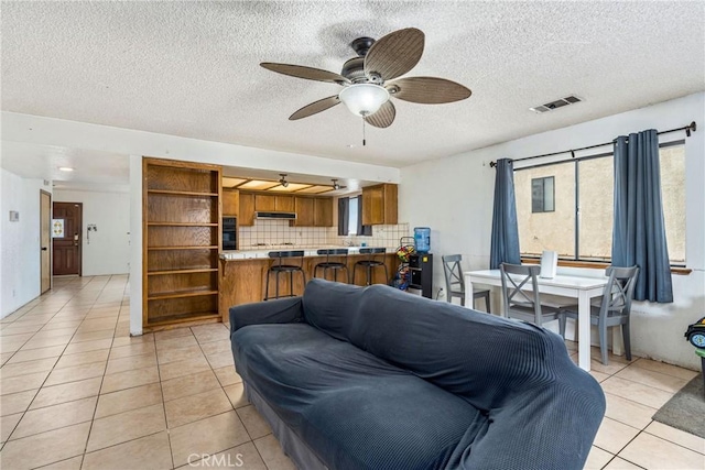 living room with a textured ceiling, light tile patterned floors, visible vents, and ceiling fan