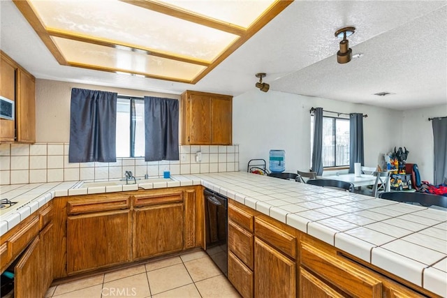 kitchen featuring light tile patterned flooring, open floor plan, brown cabinets, and dishwasher