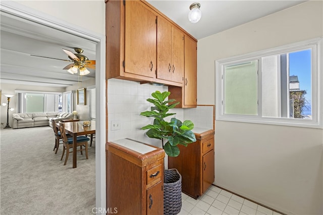 kitchen featuring ceiling fan, decorative backsplash, light countertops, light carpet, and beamed ceiling