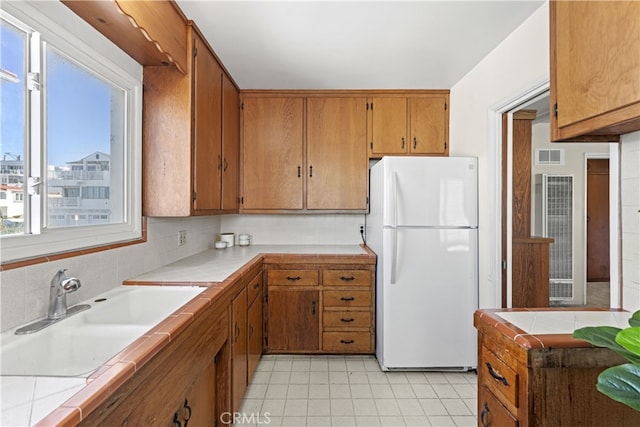 kitchen featuring visible vents, a sink, tasteful backsplash, freestanding refrigerator, and tile counters