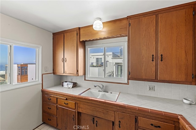 kitchen with brown cabinetry, tasteful backsplash, light countertops, and a sink