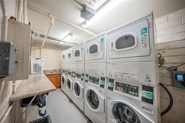 shared laundry area featuring washing machine and clothes dryer, concrete block wall, stacked washer / drying machine, and a sink