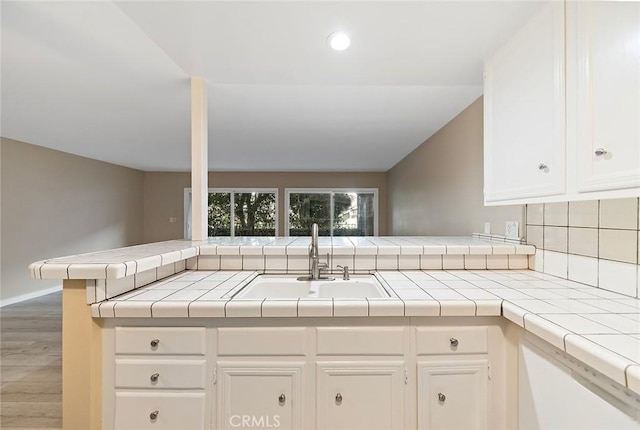 kitchen featuring white cabinetry, a peninsula, tile countertops, and a sink