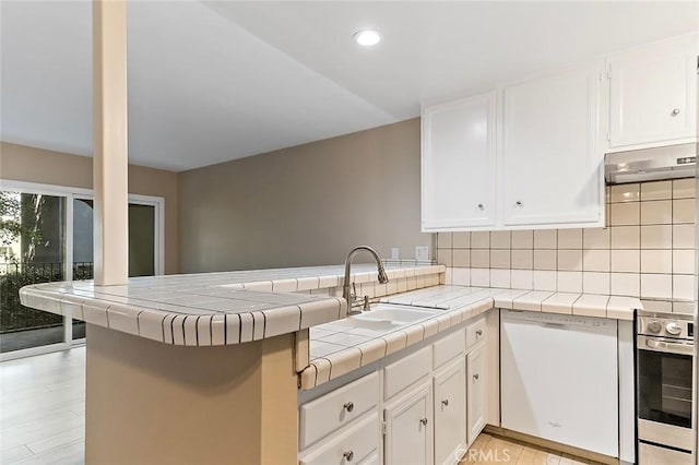 kitchen featuring wall oven, under cabinet range hood, a peninsula, white dishwasher, and a sink