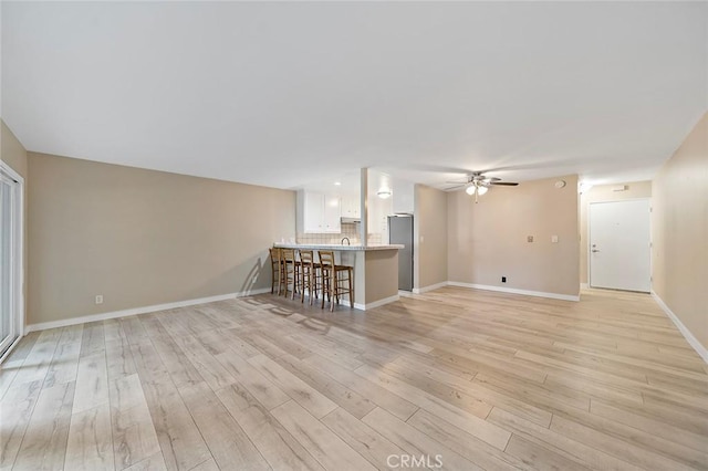 unfurnished living room featuring light wood-type flooring, baseboards, and ceiling fan