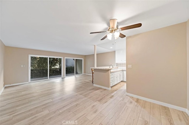 unfurnished living room featuring ceiling fan, baseboards, light wood-style floors, and a sink