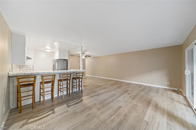 kitchen with tile countertops, a peninsula, freestanding refrigerator, ceiling fan, and a kitchen breakfast bar