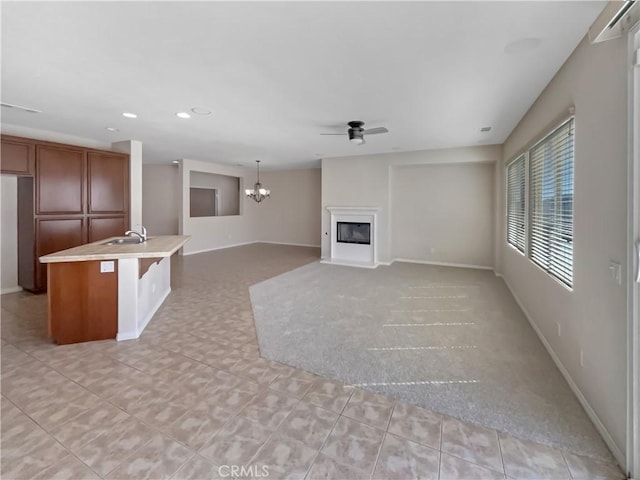 unfurnished living room with ceiling fan with notable chandelier, a sink, recessed lighting, a fireplace, and baseboards