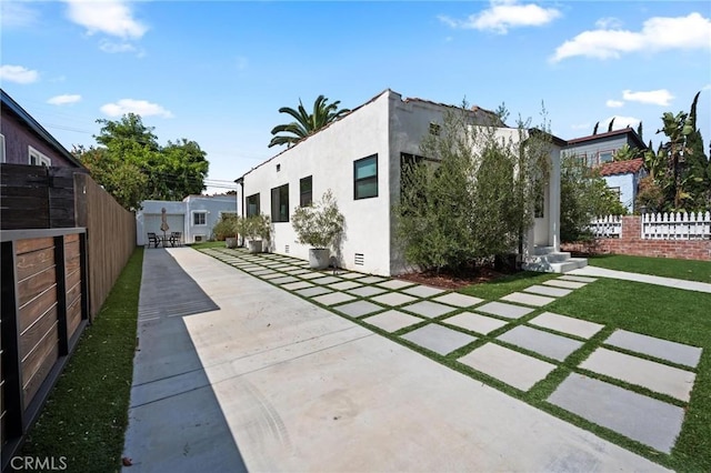 rear view of property with stucco siding, entry steps, a patio, and fence