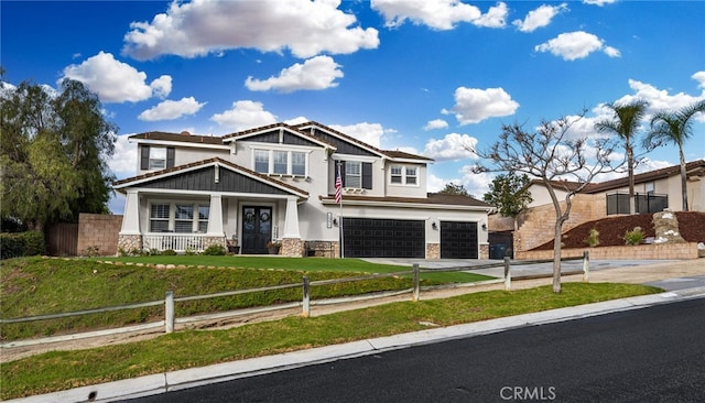 craftsman house featuring stucco siding, driveway, a fenced front yard, stone siding, and an attached garage