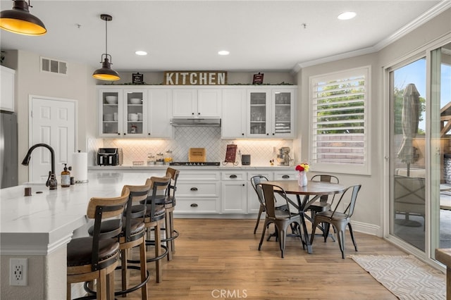 kitchen with visible vents, a sink, cooktop, under cabinet range hood, and white cabinetry