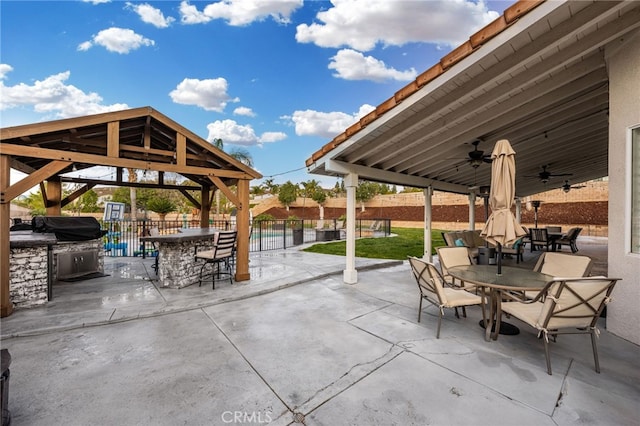 view of patio with fence, an outdoor kitchen, outdoor dining area, ceiling fan, and a gazebo