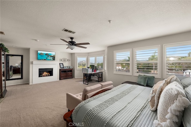 bedroom featuring visible vents, a warm lit fireplace, a textured ceiling, and carpet floors