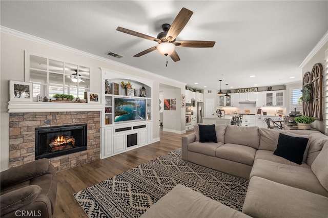 living room with visible vents, dark wood-type flooring, a stone fireplace, and crown molding