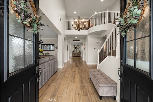 foyer entrance with light wood-style floors, a chandelier, baseboards, a towering ceiling, and stairs