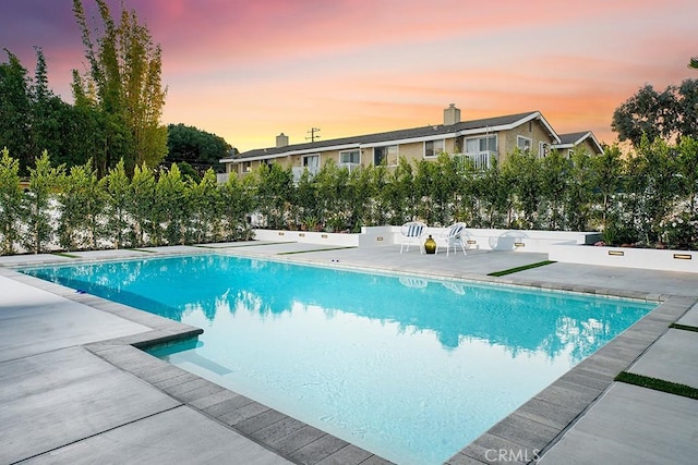 pool at dusk with an outdoor pool, a patio, and fence