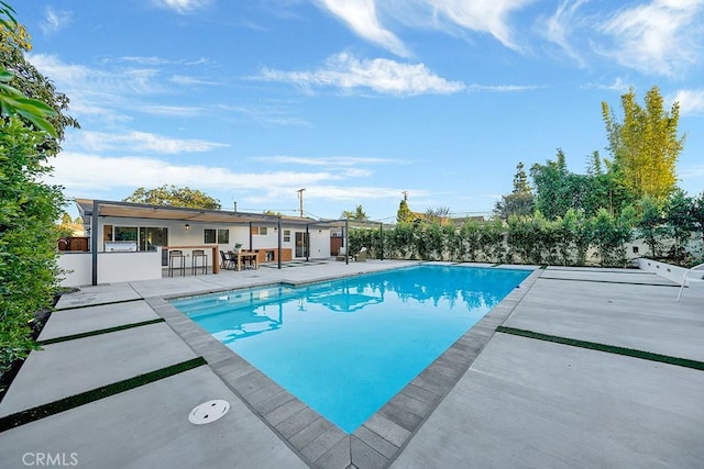 pool featuring a patio, fence, and outdoor dry bar