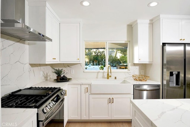 kitchen featuring a sink, white cabinetry, appliances with stainless steel finishes, wall chimney exhaust hood, and light stone countertops