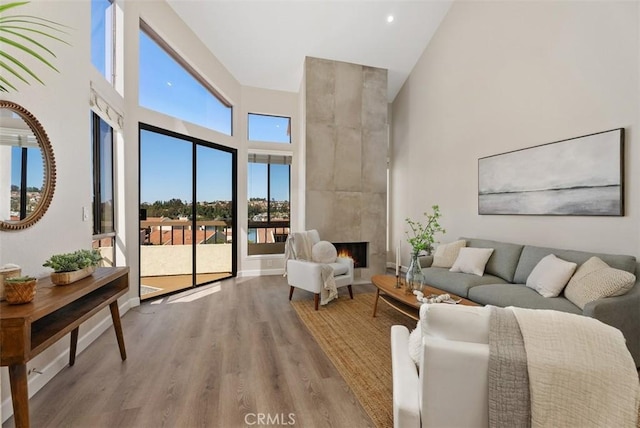 living area featuring a tiled fireplace, a high ceiling, baseboards, and wood finished floors