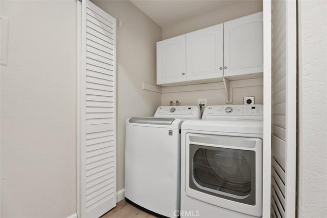 clothes washing area with cabinet space, light wood-style floors, and washing machine and clothes dryer