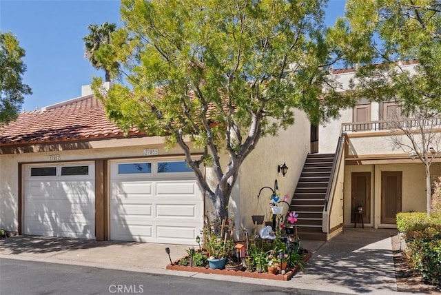 view of property with a tiled roof, stairway, a garage, and stucco siding