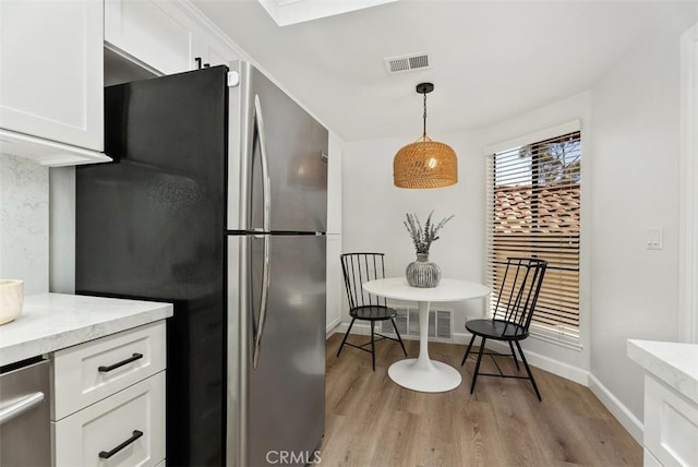 kitchen featuring visible vents, white cabinetry, freestanding refrigerator, light wood-style floors, and hanging light fixtures