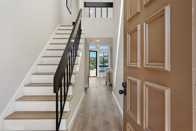 foyer entrance with baseboards, light wood-style floors, a high ceiling, and stairs