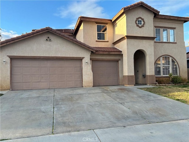 mediterranean / spanish house with a tiled roof, a garage, driveway, and stucco siding