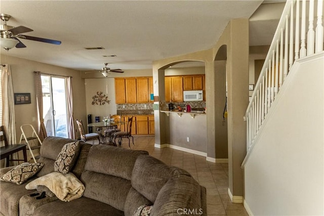 living room featuring visible vents, a ceiling fan, stairway, arched walkways, and light tile patterned floors