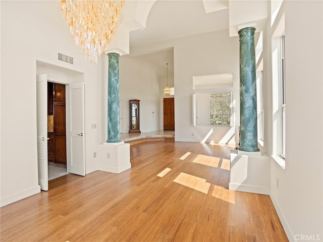 entrance foyer with visible vents, light wood-style floors, a towering ceiling, and decorative columns