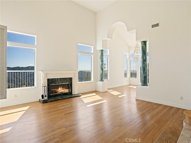 unfurnished living room with a high end fireplace, visible vents, a high ceiling, and wood finished floors