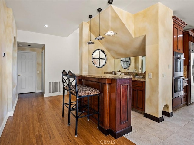 bar featuring decorative light fixtures, visible vents, baseboards, and stainless steel double oven