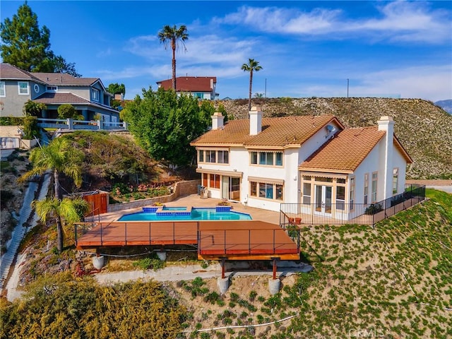 back of property with a pool with connected hot tub, a tile roof, stucco siding, a chimney, and a patio area