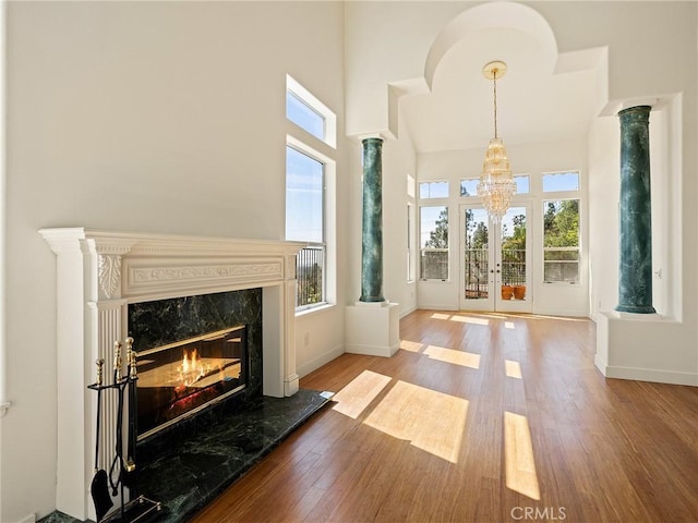 living area featuring a high end fireplace, a healthy amount of sunlight, decorative columns, and wood finished floors