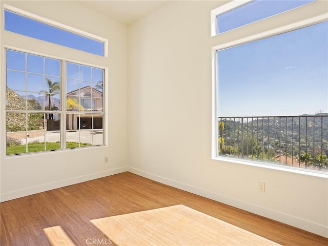 unfurnished room with plenty of natural light, wood finished floors, and baseboards