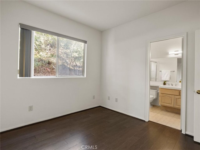 unfurnished bedroom featuring dark wood finished floors, connected bathroom, baseboards, and a sink