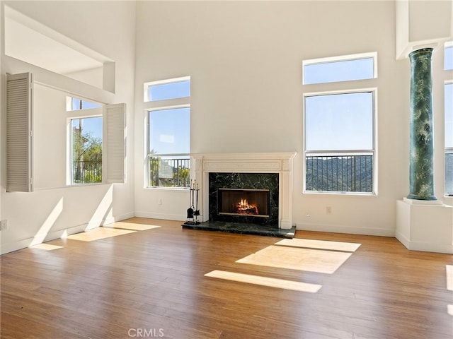 unfurnished living room with a premium fireplace, baseboards, a towering ceiling, and wood finished floors