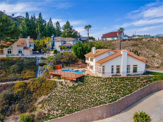 back of property with fence, a fenced in pool, a chimney, stucco siding, and a residential view