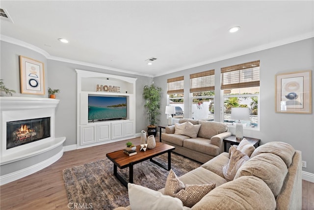 living area with a glass covered fireplace, wood finished floors, visible vents, and ornamental molding