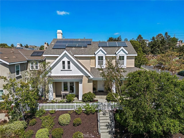 view of front of home featuring a fenced front yard, solar panels, a chimney, and a shingled roof