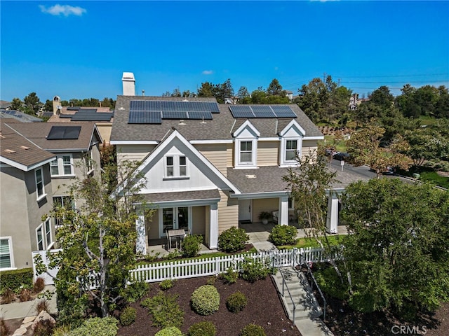 view of front facade featuring a chimney, solar panels, a shingled roof, and fence