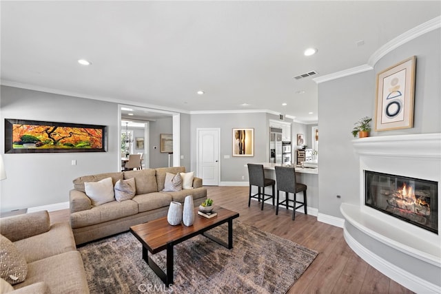 living room featuring wood finished floors, visible vents, recessed lighting, a glass covered fireplace, and crown molding