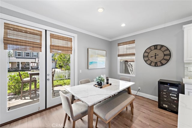 dining room featuring beverage cooler, baseboards, light wood-style floors, french doors, and crown molding