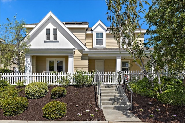 view of front facade with a porch, a fenced front yard, and roof mounted solar panels