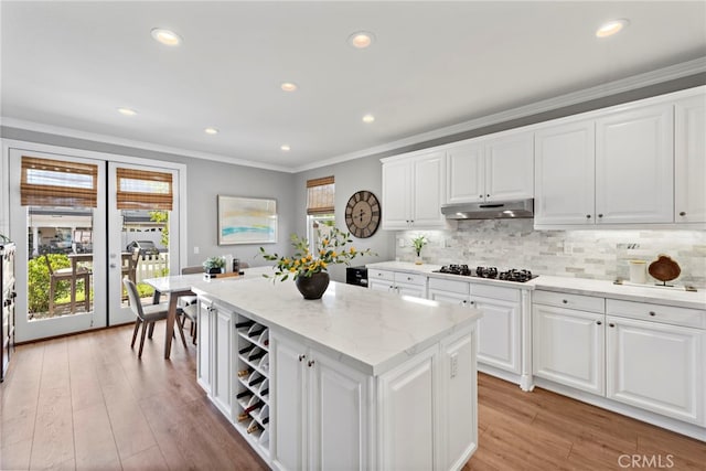 kitchen with under cabinet range hood, decorative backsplash, light wood finished floors, and crown molding