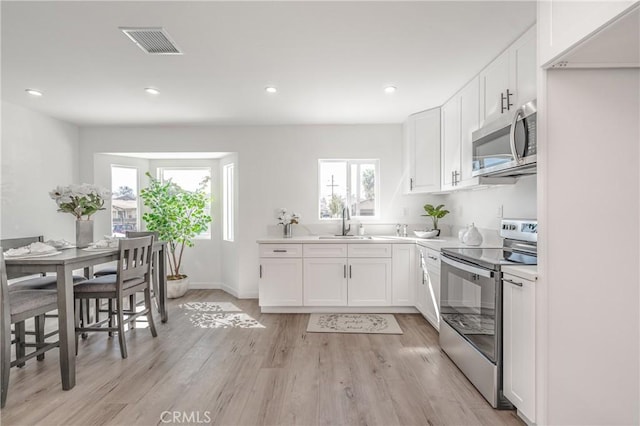 kitchen featuring visible vents, appliances with stainless steel finishes, light wood-style floors, white cabinets, and a sink